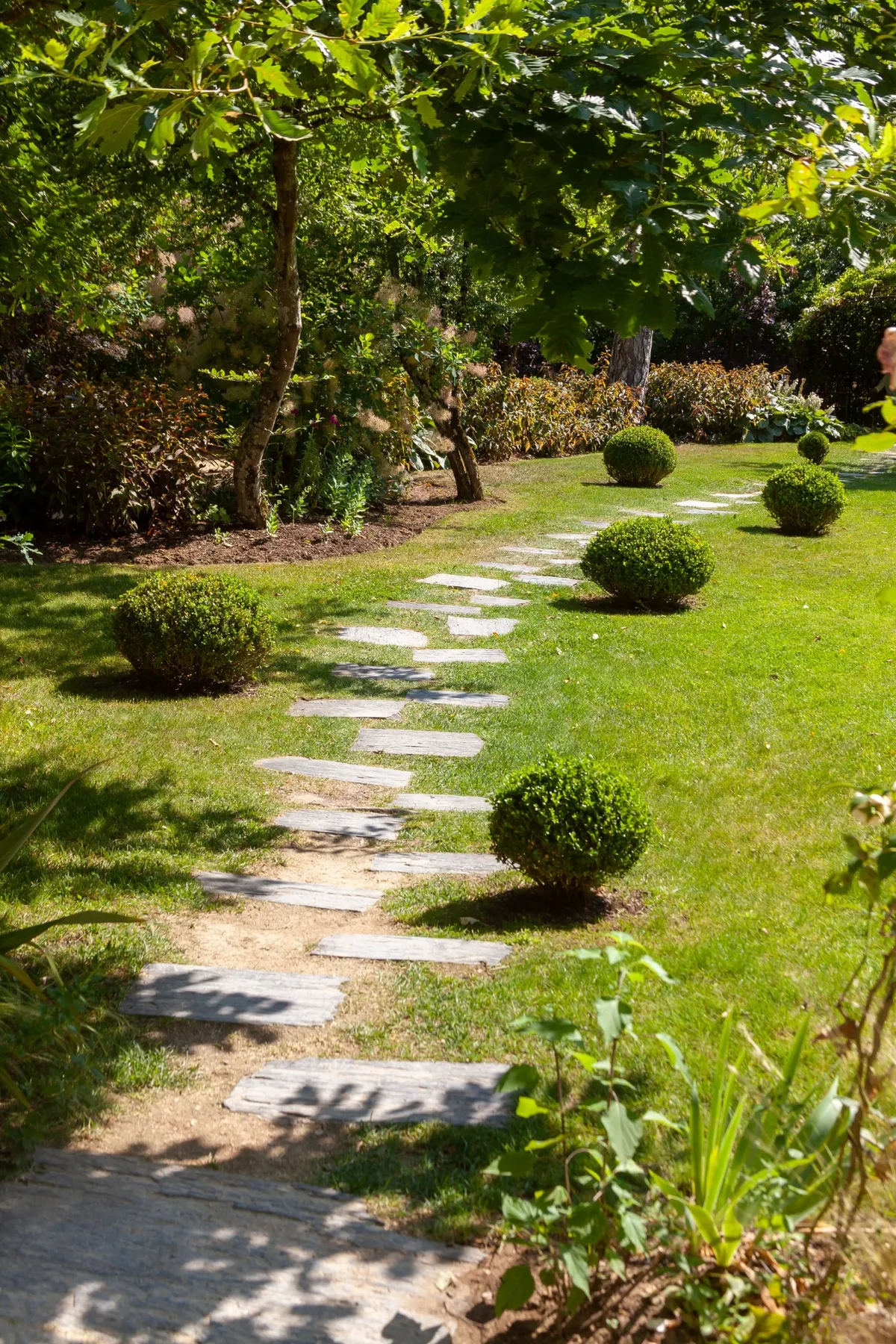 Allée en dalles entourée de pelouses bien entretenues et de petits arbustes dans un jardin paysager.